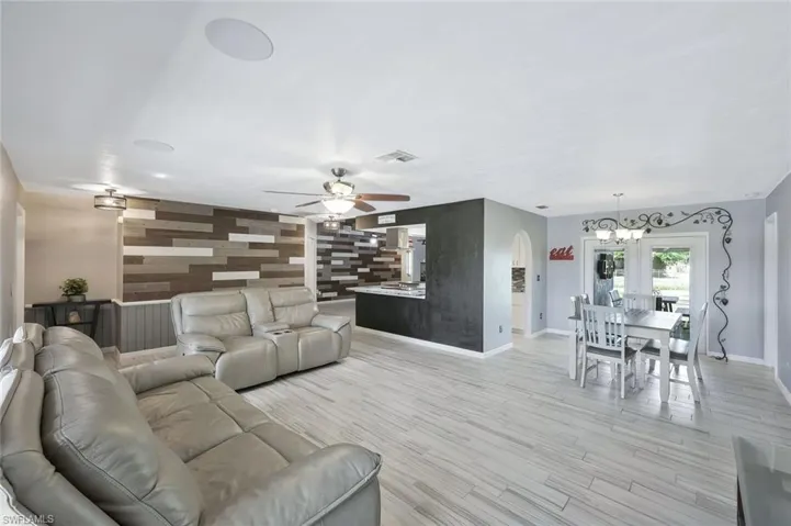 Living room featuring visible vents, ceiling fan with notable chandelier, arched walkways, light wood-style floors, and an accent wall