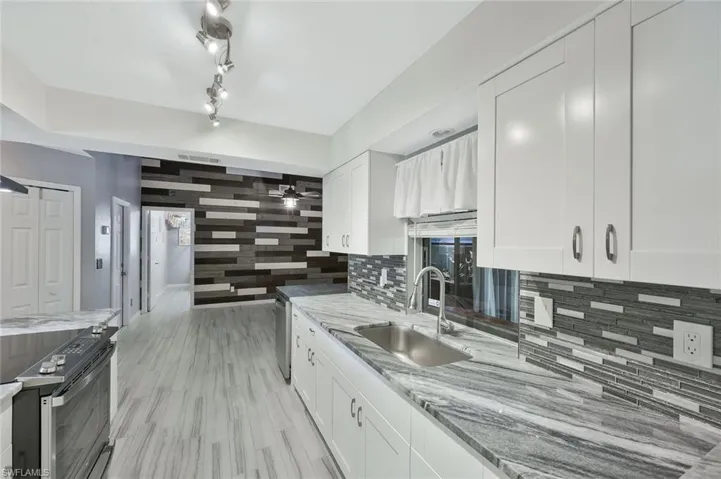 Kitchen with a sink, stainless steel appliances, decorative backsplash, and white cabinetry