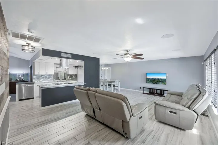 Living room featuring visible vents, ceiling fan with notable chandelier, light wood-style floors, and lofted ceiling