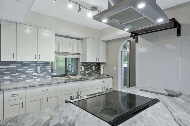 Kitchen with backsplash, light stone countertops, arched walkways, white cabinetry, and a sink