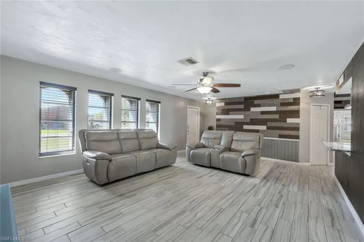 Living area featuring light wood-style floors, a ceiling fan, visible vents, and baseboards