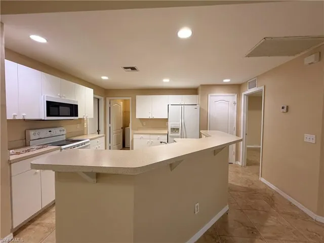 Kitchen featuring white cabinets, a kitchen bar, light countertops, white appliances, and a large island