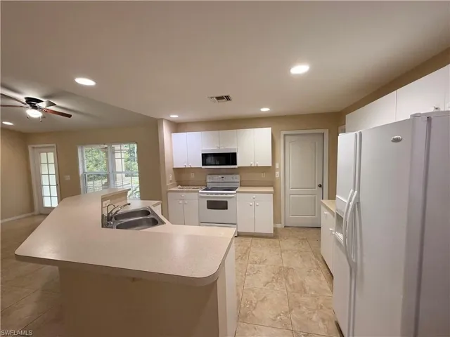 Kitchen featuring white appliances, a center island with sink, light countertops, white cabinetry, and ceiling fan