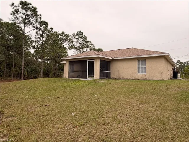 Back of property featuring stucco siding, a sunroom, a yard, and roof with shingles