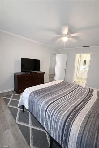 Bedroom with crown molding, ensuite bath, a ceiling fan, and wood finished floors