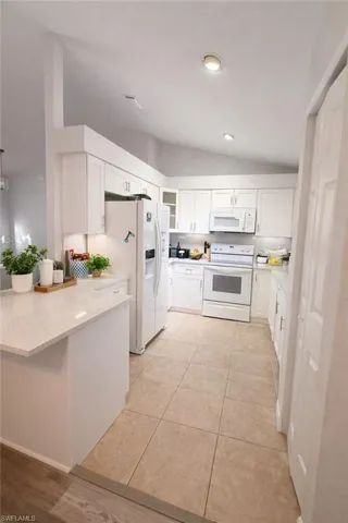 Kitchen with vaulted ceiling, white cabinets, white appliances, light stone countertops, and light tile patterned flooring