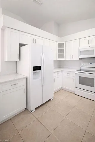 Kitchen with white appliances, white cabinets, glass fronted cabinets, and light tile patterned floors
