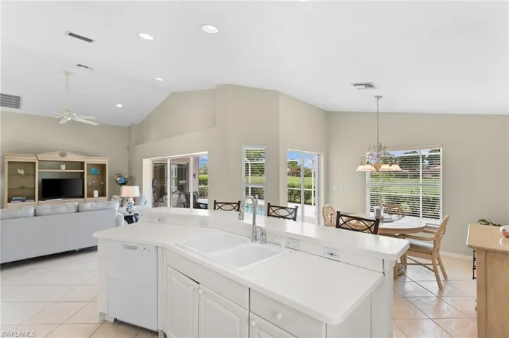 Kitchen featuring ceiling fan with notable chandelier, white dishwasher, sink, a center island with sink, and white cabinetry