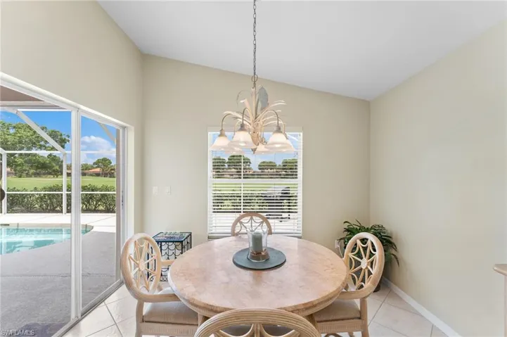 Tiled dining area featuring a healthy amount of sunlight, vaulted ceiling, and an inviting chandelier