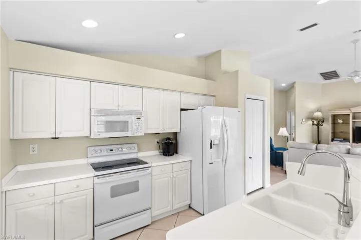 Kitchen featuring white appliances, white cabinets, sink, vaulted ceiling, and light tile patterned floors