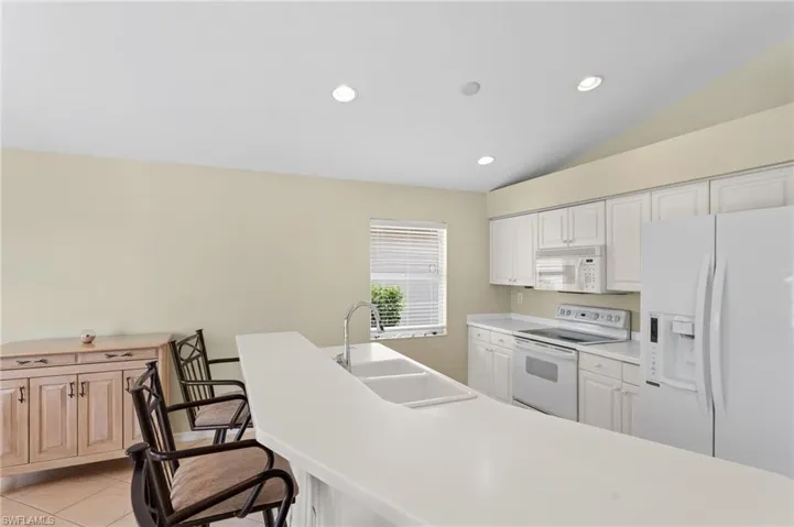 Kitchen featuring sink, light tile patterned floors, lofted ceiling, white appliances, and white cabinets