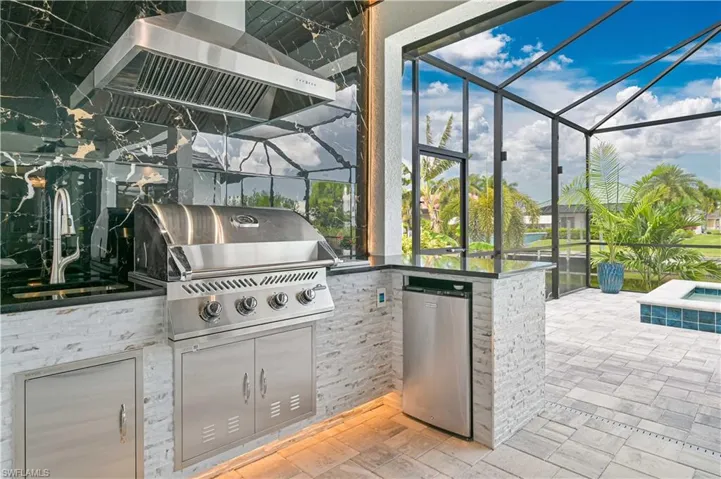 Outdoor kitchen featuring a stainless steel grill, coordinating ventilation hood, and black stone backsplash