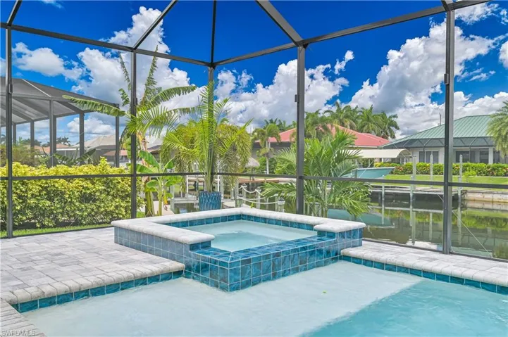 Screened enclosure featuring an integrated hot tub with blue ceramic tile, a light-colored tiled pool, and a paver patio