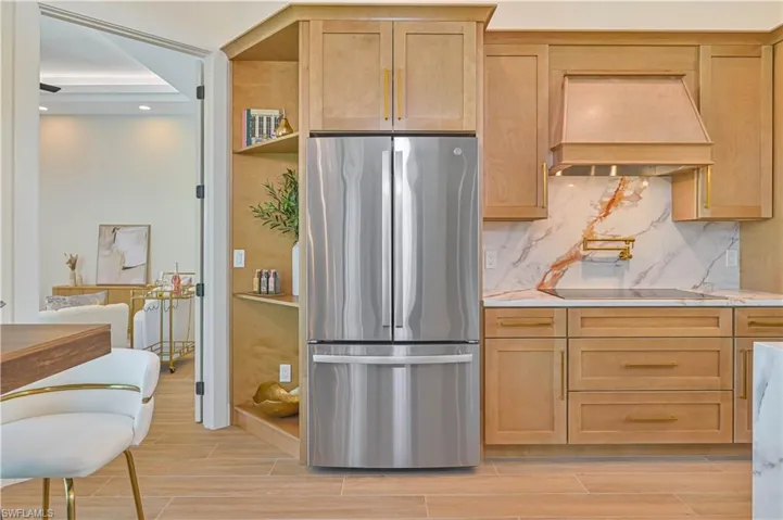 Gourmet kitchen featuring light wood cabinetry with gold-tone hardware, a stainless steel refrigerator, and a smooth cooktop