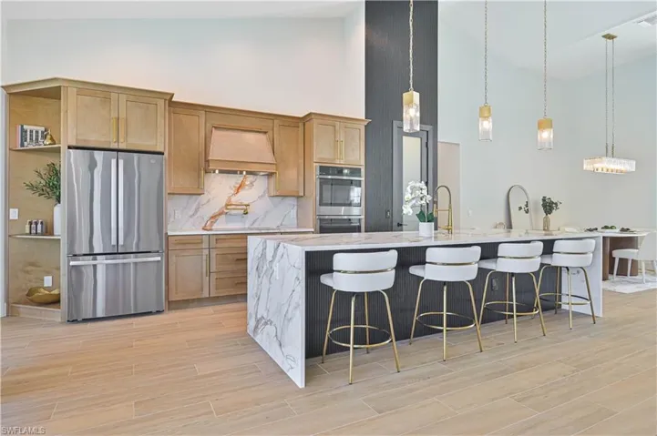 Modern kitchen featuring a waterfall island with a light-toned countertop, a built-in stainless steel refrigerator, light wood-finish cabinetry, a matching wood-finish range hood, and plank-style flooring