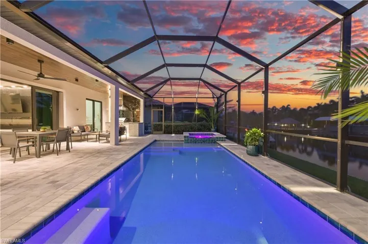 Screened outdoor living area featuring a rectangular pool with integrated lighting, an elevated spa, a covered patio with an outdoor kitchen, and a waterfront setting