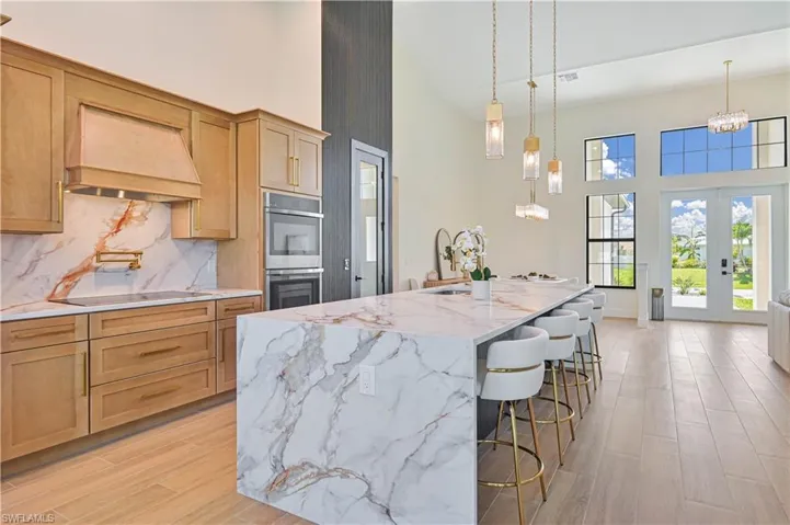 Contemporary kitchen featuring an expansive waterfall island with seating, integrated cooktop, dual wall ovens, and custom wood cabinetry