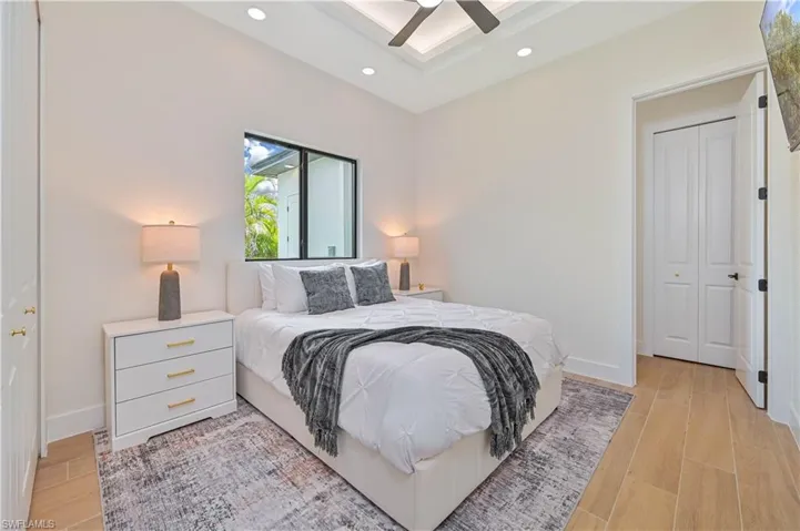 Bright room featuring a recessed tray ceiling with a ceiling fan, a large window with black framing, and light wood-finish flooring
