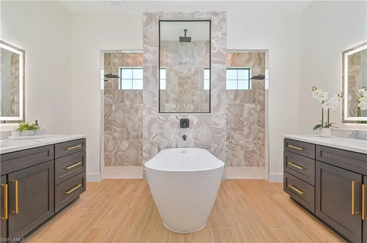Freestanding soaking tub with a floor-mounted faucet, flanked by dual walk-in showers with rain showerheads