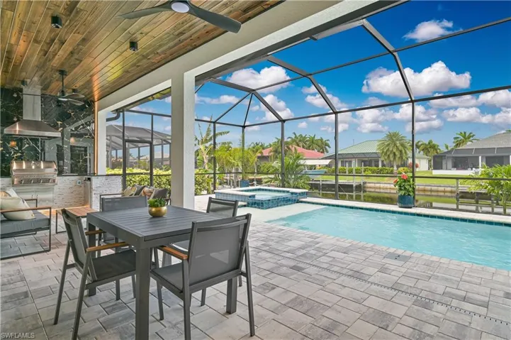 Screened lanai featuring a swimming pool, integrated spa, and an outdoor kitchen with a built-in grill and vent hood