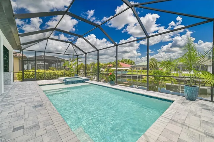 Screened lanai featuring a swimming pool, integrated spa, and grey paver decking