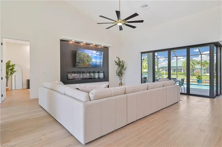 Vaulted ceiling living area featuring wood-finish flooring, a contemporary ceiling fan, and a built-in media wall with integrated lighting