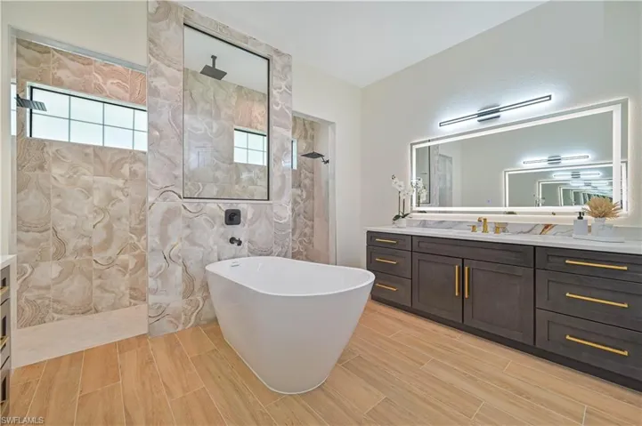 Freestanding soaking tub with a wall-mounted faucet, dual rainfall shower heads, and wood-finish flooring