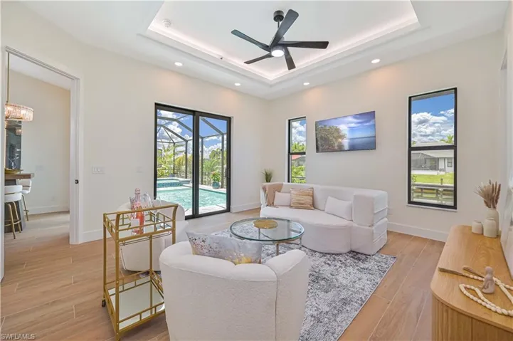 Living area featuring wood-look tile flooring, a tray ceiling with recessed lighting and a ceiling fan, and large windows