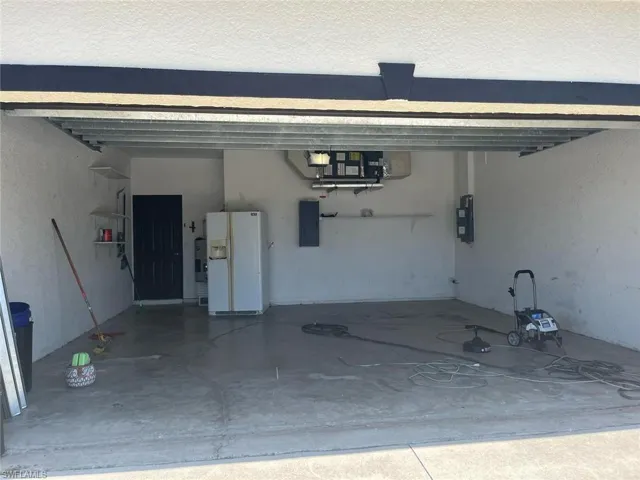 Garage featuring white fridge with ice dispenser and electric panel