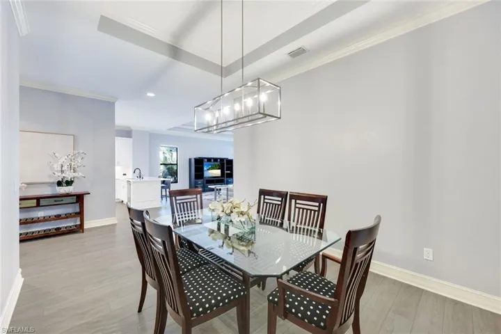 Dining space with a tray ceiling, crown molding, light wood-style flooring, and an inviting chandelier