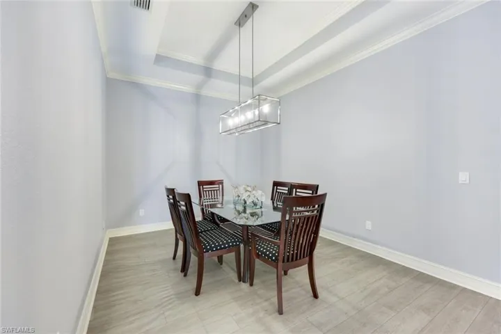 Dining space with a tray ceiling, crown molding, light wood-style flooring, and an inviting chandelier