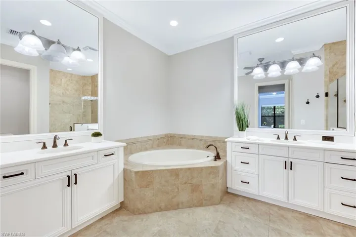 Primary bathroom with tile patterned floors, white cabinetry, quartz counters, soaking tub and frameless shower door