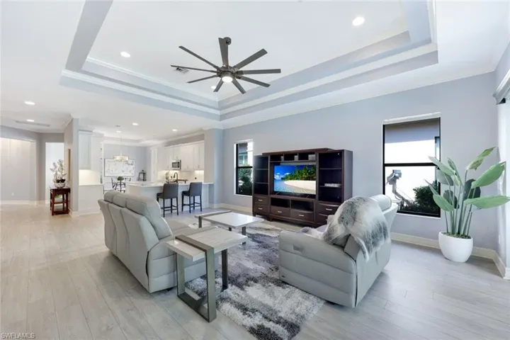 Living room featuring a tray ceiling, crown molding, ceiling fan, and light wood-style floors