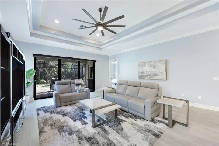 Living room featuring a tray ceiling, crown molding, ceiling fan, and light wood-style floors