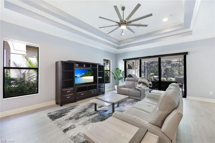 Living room featuring a tray ceiling, crown molding, ceiling fan, and light wood-style floors