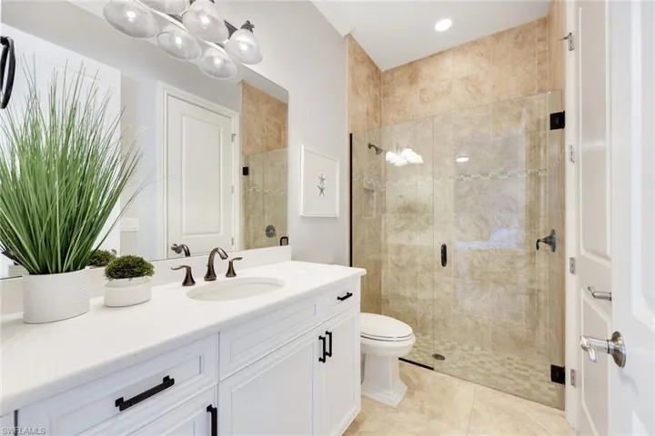 Bathroom with tile patterned floors, white cabinetry, quartz counters and frameless shower door