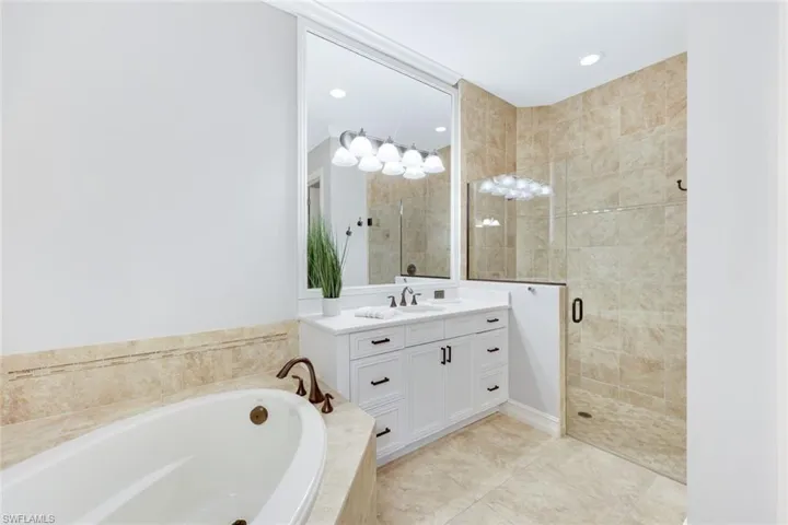Primary bathroom with tile patterned floors, white cabinetry, quartz counters, soaking tub and frameless shower door
