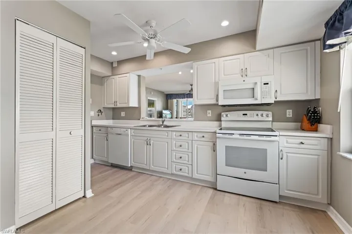 Kitchen with white appliances, light countertops, white cabinetry, a ceiling fan, and light wood finished floors