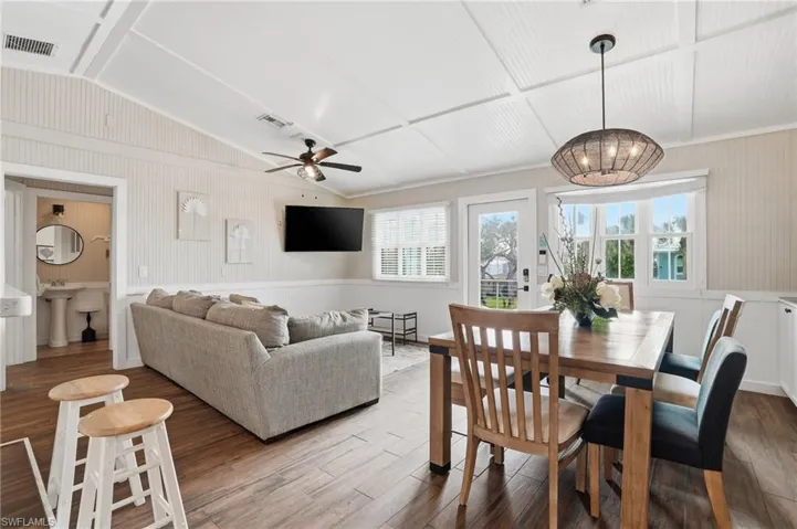 Dining area featuring wood finished floors, lofted ceiling, a ceiling fan, a wainscoted wall, and a chandelier - Virtually Edited Image