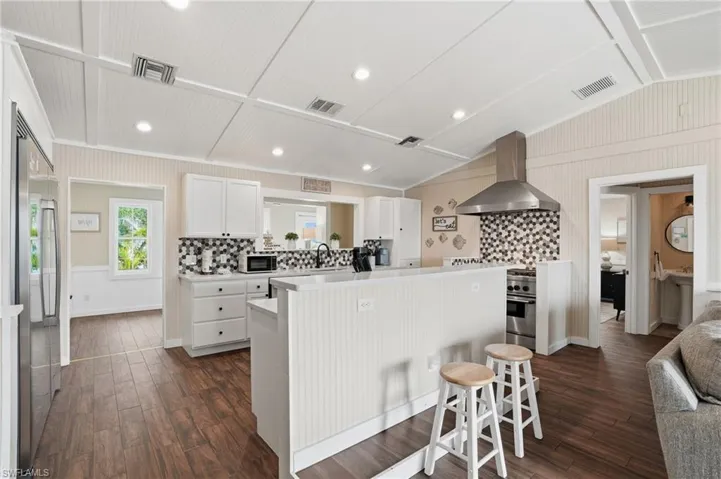 Kitchen with white cabinets, decorative backsplash, light countertops, wall chimney exhaust hood, and dark wood-type flooring - Virtually Edited Image