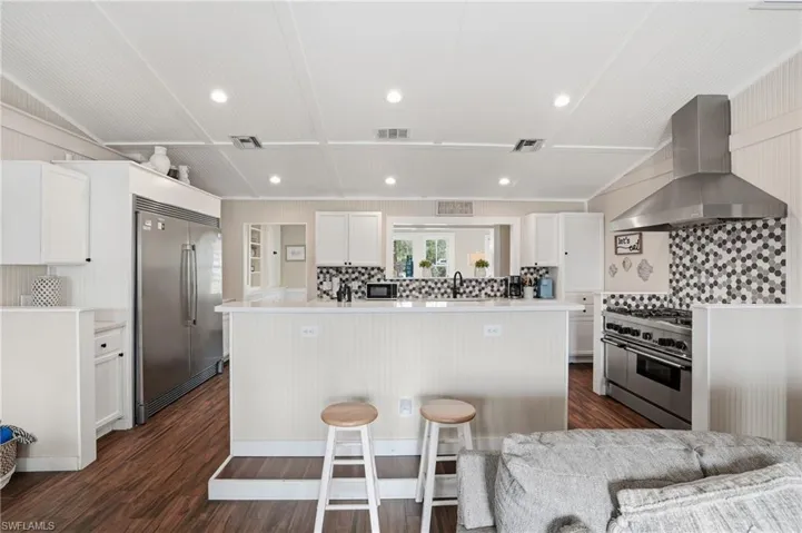 Kitchen with wall chimney exhaust hood, white cabinets, high quality appliances, recessed lighting, and decorative backsplash - Virtually Edited Image