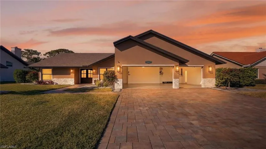 View of front of property with stucco siding, a yard, decorative driveway, stone siding, and a garage