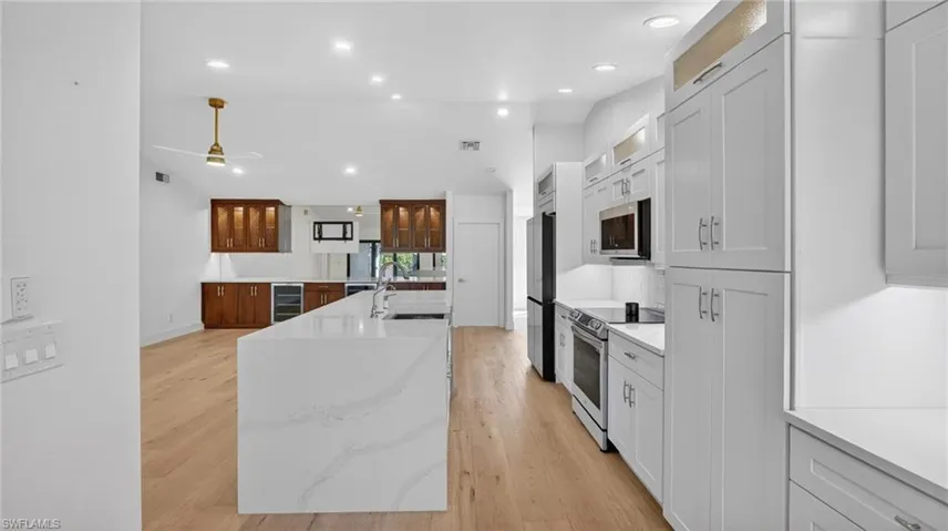 Kitchen featuring glass insert cabinets, a kitchen island with sink, stainless steel appliances, light wood-style flooring, and light stone counters