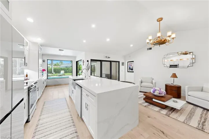 Kitchen featuring white cabinets, open floor plan, light stone countertops, vaulted ceiling, and light wood-type flooring