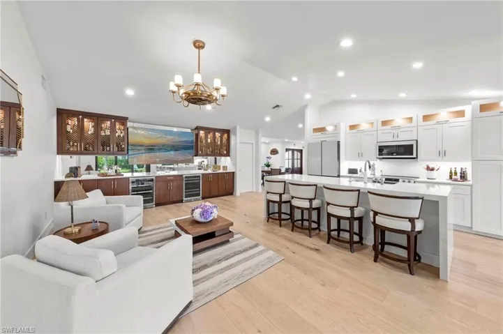 Living room with light wood-style floors, lofted ceiling, a chandelier, wine cooler, and recessed lighting