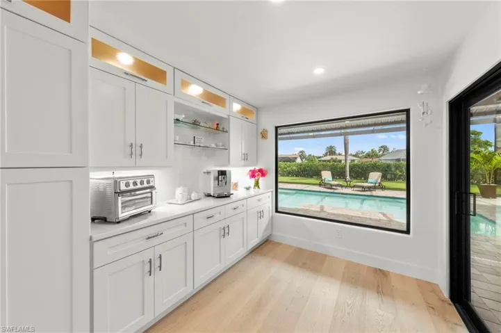 Bar area featuring white cabinets, light wood-style floors, glass insert cabinets, recessed lighting, and light stone countertops