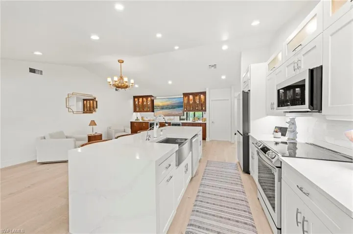 Kitchen with white cabinets, appliances with stainless steel finishes, light wood-style floors, recessed lighting, and lofted ceiling