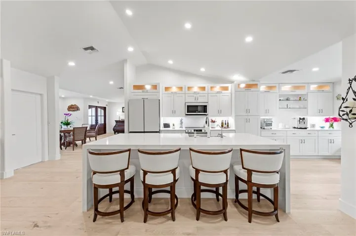 Kitchen featuring white cabinets, glass insert cabinets, a spacious island, vaulted ceiling, and recessed lighting