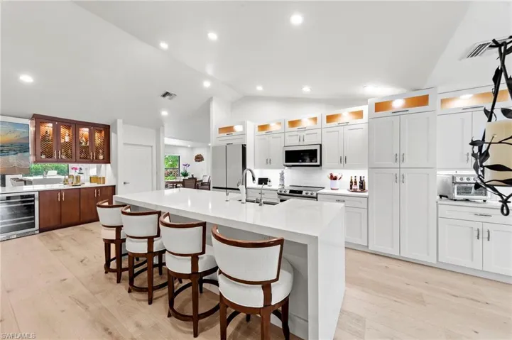 Kitchen with glass insert cabinets, a breakfast bar, light stone counters, beverage cooler, and a kitchen island with sink