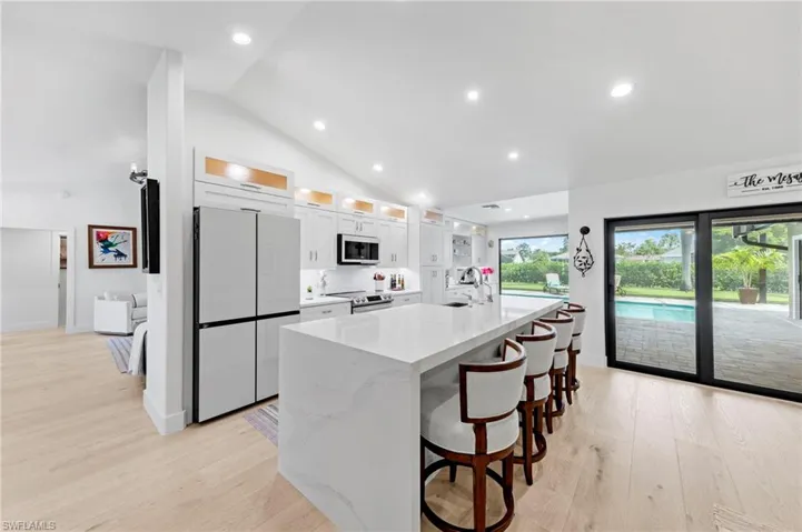 Kitchen with glass insert cabinets, a breakfast bar area, white appliances, light stone countertops, and light wood finished floors